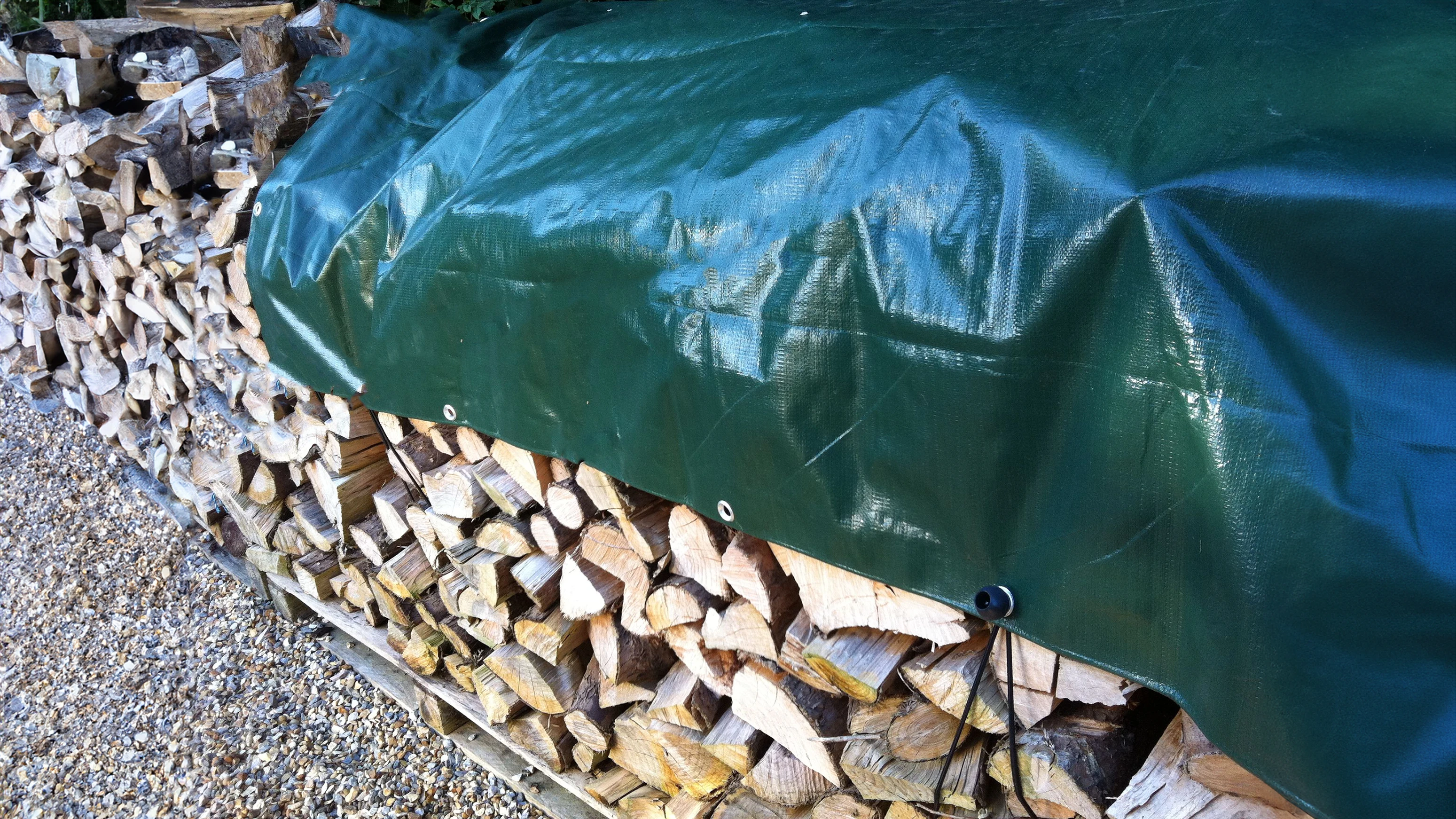 Green tarpaulin securely covering a stacked log store
