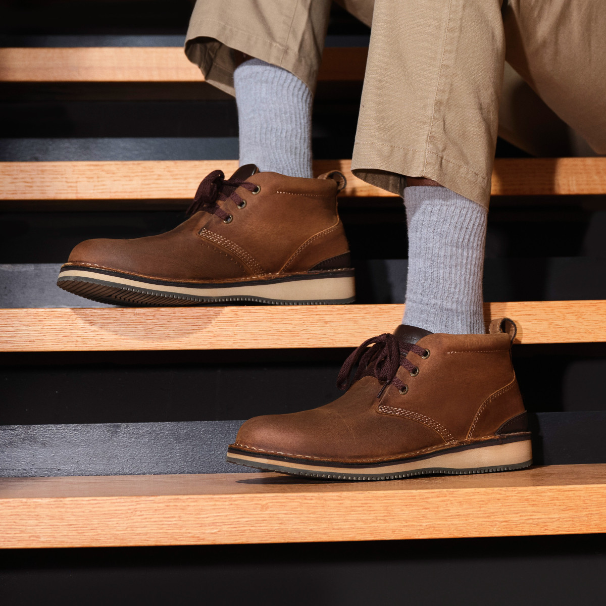  Man wearing brown leather chukka work boots with gray socks and khaki pants, standing on wooden steps