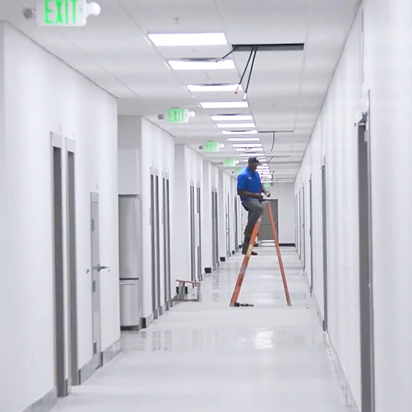 Powerful Signal installer on a ladder pulling cable above a corridor ceiling