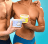 Two shirtless male models standing side-by-side against a light blue background, each holding a container of Boy Butter lubricant (one blue label, one yellow label). The focus is on the product in their hands with their torsos visible.