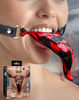 The Dragon’s Lick Vibrating Demon Tongue shown worn in the mouth with the adjustable black harness secured around the face. The red-and-black sculpted tongue extends outward with textured barbed detailing. Product packaging is visible in the lower corner.