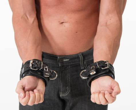 Model wearing matching leather wrist and ankle cuffs set, demonstrating full restraint positioning and hardware