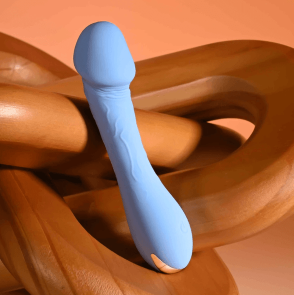 Dainty Dick Vibe side-angle product image showing a compact blue vibrator with a narrow flexible shaft, curved tip, and rounded base against a brown background.