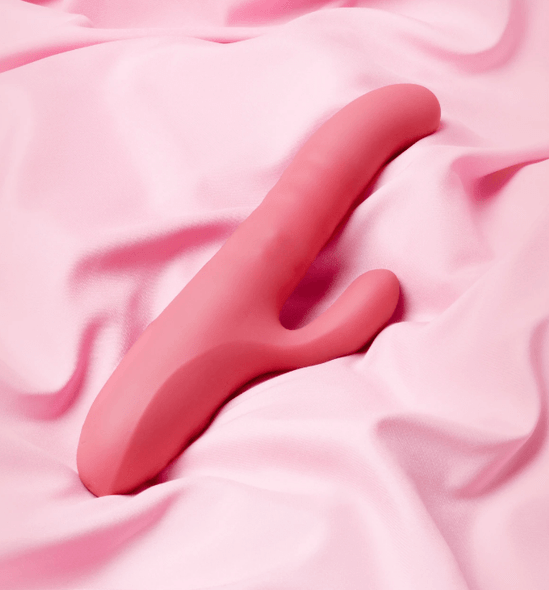 Close-up of the Le Wand Thrust Rabbit Vibrator displayed over pink satin sheets, highlighting the curved insertable shaft, rounded tip, and external clitoral arm, with focus on the toy’s dual-arm profile and control interface.