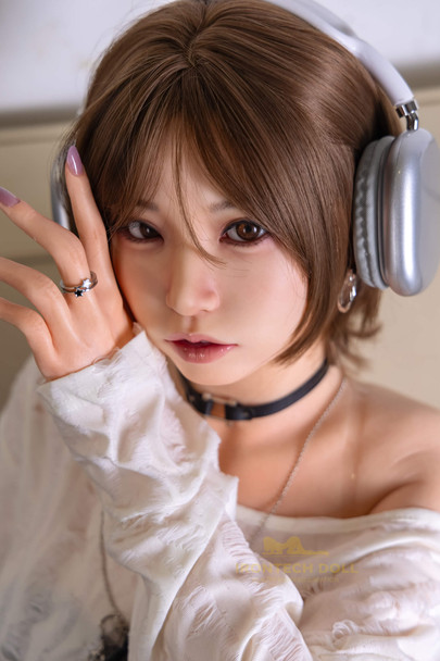 Close-up of Suki sex doll with short brown hair, brown eyes, pink lips and hands posed beside her face.