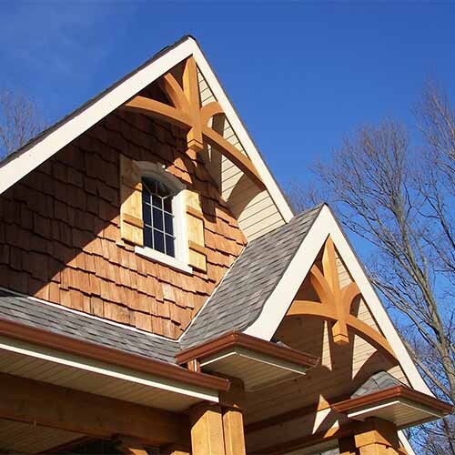 Cedar-shingled gable with arched window, decorative timber brackets, gray roof, blue sky