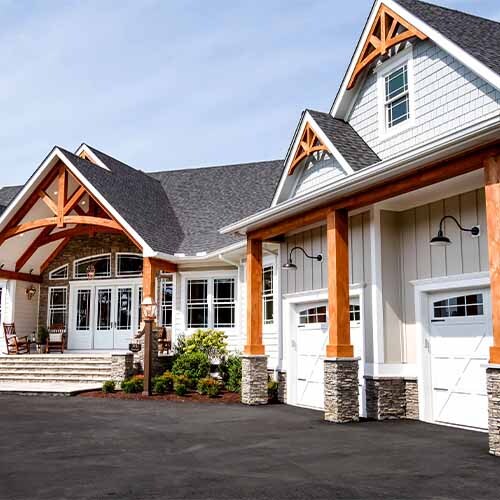 Large modern craftsman house exterior featuring a grand covered porch with exposed timber framing, stone column bases, light vertical siding, and multiple gables.