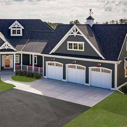 Gray farmhouse with decorative gable brackets over front porch and three-car garage