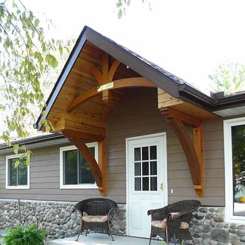 Thick, exposed timber columns support a covered porch entryway and features a prominent gable roofline and dark railings.