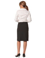 A black wool stretch pleated skirt, seen from the back, paired with a white shirt and heeled shoes.