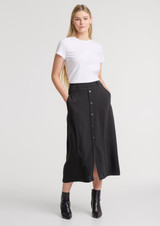 A woman wears a black midi skirt with a front slit and buttons, paired with a simple white T-shirt.