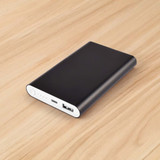 A black power bank with a sleek design, featuring USB ports and a power indicator, placed on a wooden surface.