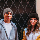 Two people wearing woolly beanies, one in grey and the other in black, standing in front of a metallic gate.