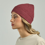 A maroon ribbed beanie worn by a model with wavy hair, facing to the side. The product has a logo.