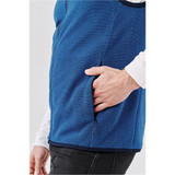 A blue vest featuring a side pocket, worn over a white long-sleeve shirt. It has a sleek design and casual style.