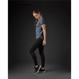 A woman in a navy crew neck t-shirt and black leggings stands in profile against a dark background.