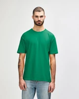 A man wearing a green Gildan Softstyle adult t-shirt, standing against a plain background, paired with blue jeans.