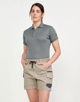 A woman wearing unisex cotton stretch drill shorts in beige, paired with a grey polo shirt. The shorts feature pockets and a drawstring.