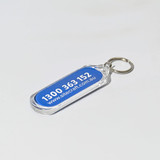 An oval acrylic keychain with a transparent border and a blue interior featuring a logo and phone number.