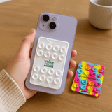 A purple phone held in hand with a white suction phone wallet on the back and two colourful cards beside it.