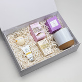 A gift box containing a grey pottery cup, drinking chocolate, marshmallows, and assorted skincare items.