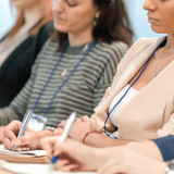 A group of people sitting at a table, writing in notebooks with various pens, including metal pens.