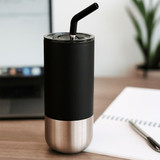 A drink bottle featuring a black matte finish and stainless steel bottom, with a black straw and a lid, beside a notebook and laptop.