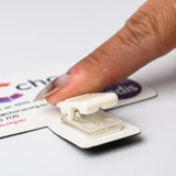 A T-Magnet with a white clip, featuring a logo, is held by a finger against a white surface.
