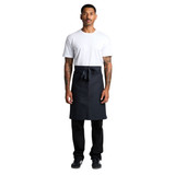 A man in a white t-shirt wears a dark grey Carrie Half Apron, with a tied waist and a logo on the apron.