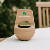 A wireless speaker in plant fibre, featuring a rounded design with a light brown colour and a logo on the front.