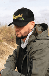 A black cap with a mesh back features a logo and is worn by a person in a green jacket outdoors.