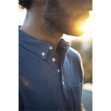 A men's polo shirt in blue with a collar, buttons, and a chest pocket, featuring soft lighting effects.