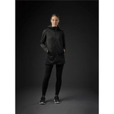 A woman wearing a black Women's Belcarra Softshell jacket, paired with black leggings and sneakers. The jacket features a hood and pockets.