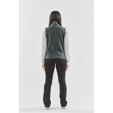 A woman stands with her back to the camera, wearing a grey fleece vest over a long-sleeved shirt, paired with black pants.