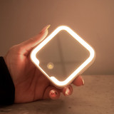 A compact mirror with an LED light in a square shape, held in a hand, featuring a sleek design.