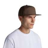 A brown 7-panel cap with a flat brim, featuring a logo, worn by a model in a white T-shirt.