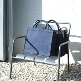 Navy blue recycled tote bags are displayed on a metal chair against a light brick wall. One bag is slightly behind the other.