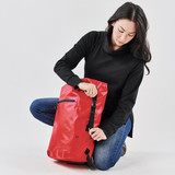 A red backpack with a sleek design, featuring a zippered pocket and adjustable straps, held by a person in black attire.
