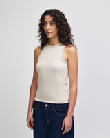 A fitted tank top in a light beige colour, featuring a high neckline and worn with dark jeans. The model has curly hair.