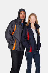 A grey and navy rain jacket featuring orange and red accents, displayed on a male and female model with hoods.