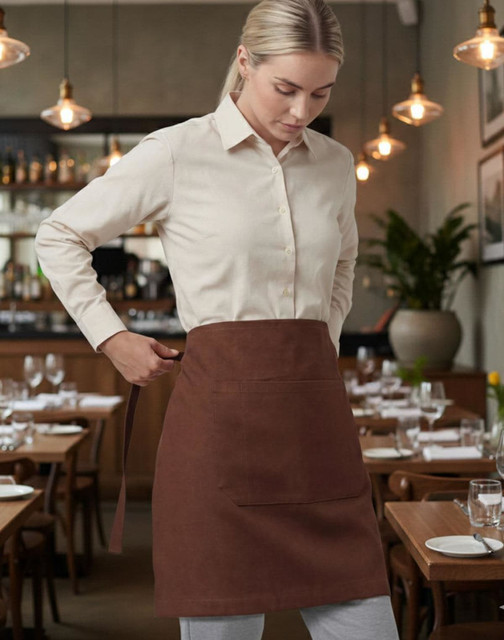 A grey canvas short waist apron in black worn by a person facing another person in casual attire against a brick wall.