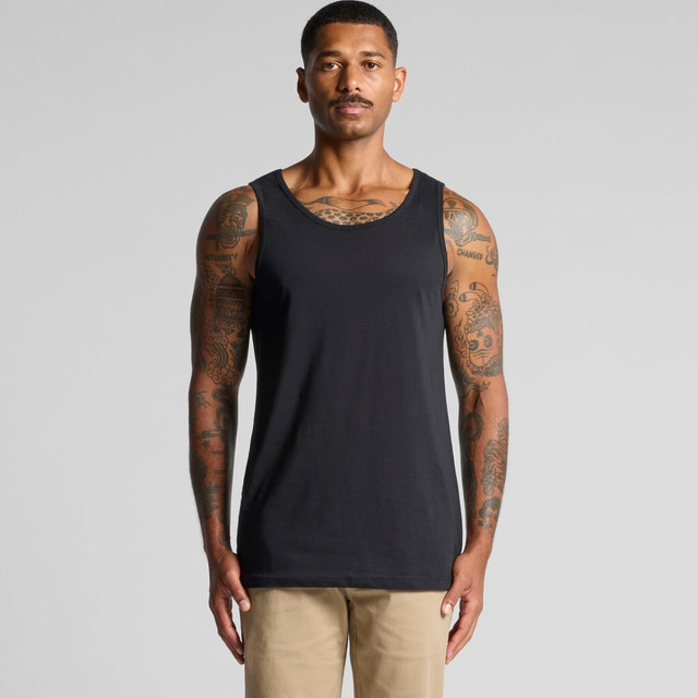 A man with tattoos wearing a plain black singlet. The singlet has a round neckline and minimal design.