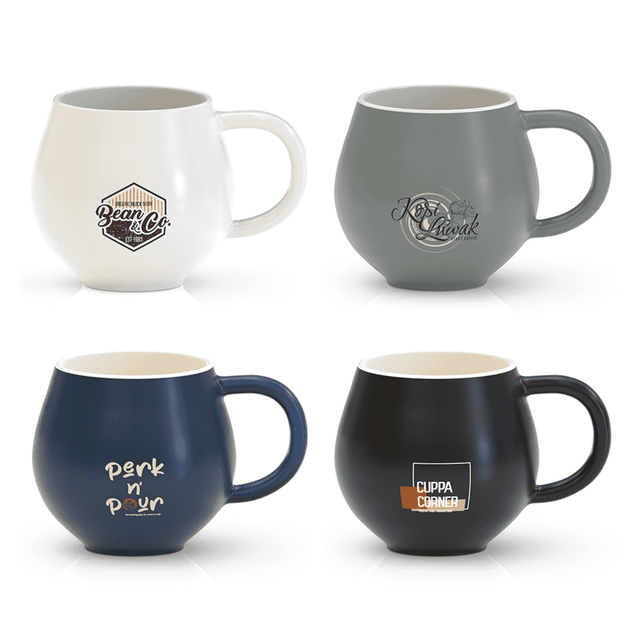 A collection of four coffee mugs in white, grey, navy, and black, each with distinctive branding.