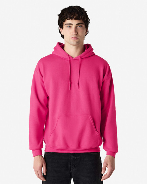 A pink Gildan Heavy Blend adult hooded sweatshirt with a front pocket and a hood. The model stands in a neutral background.