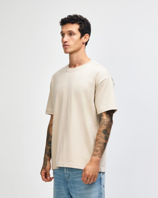 A beige super heavyweight T-shirt displayed on a model, featuring a relaxed fit and short sleeves.