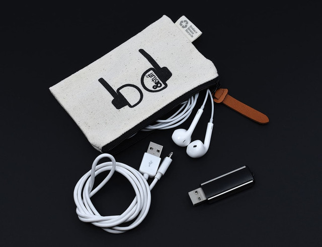 A calico earphone pouch with black graphics, containing white earphones, USB cables, and a USB drive.