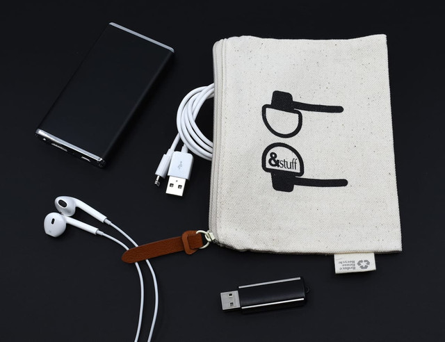 A neutral calico earphone pouch with a logo, surrounded by earphones, USB cables, and a portable charger.