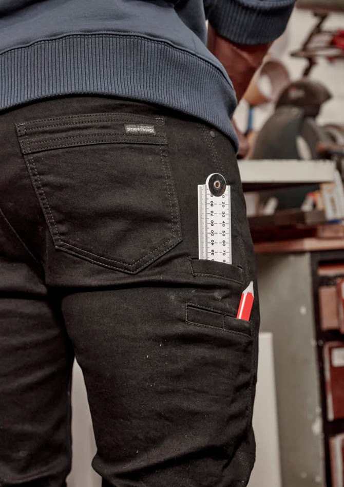 A pair of black stretch jeans with tool pockets and a ruler visible in one pocket, featuring a logo on the back.
