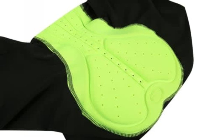 A close-up of black cycling shorts featuring a bright green padded chamois with ventilation holes.
