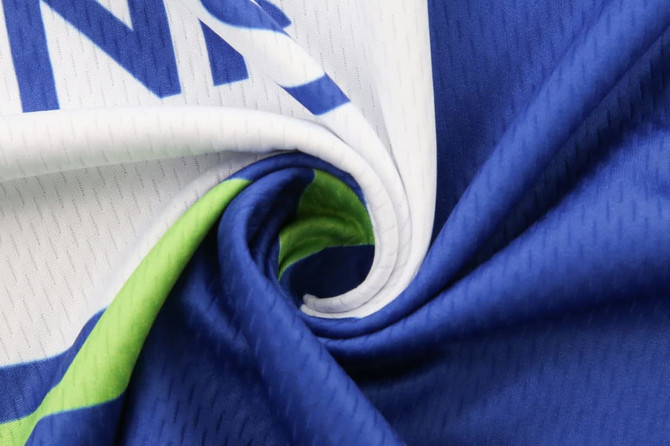 A close-up of a blue and white sports uniform fabric, featuring a swirl of material with a green inner lining and a logo.